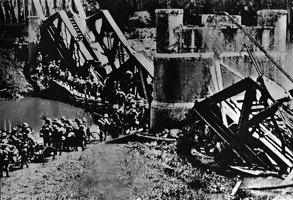 Japanese troops pass a destroyed railroad bridge as they enter Burma from neighboring Thailand
